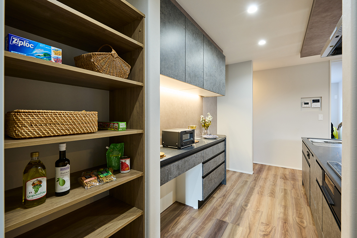 Modern kitchen with open wooden pantry shelves on the left wicker baskets and bottles on the lower shelves gray cabinets line the back wall with under cabinet lighting and a toaster oven on the counter